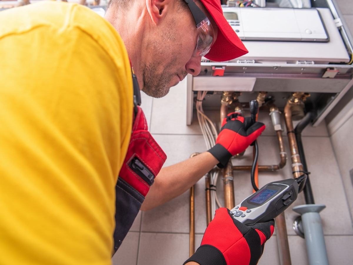 Un technicien en tenue de travail relève une mesure à l'appareil portatif sur les tuyauteries d'une chaufferie